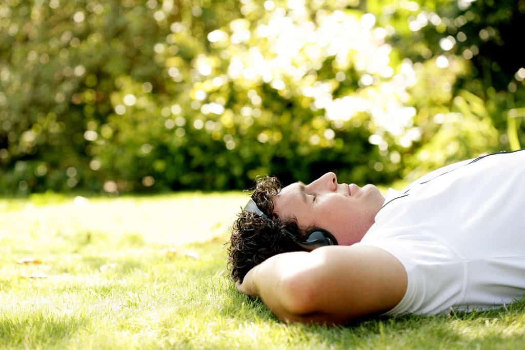 Man laying on the grass listening to an audible alternative audiobook